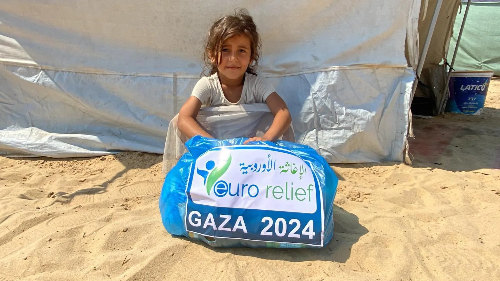 A child sits with a Euro Relief food parcel outside a tent